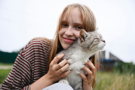 A smiling girl is petting her cat outdoors in summer
