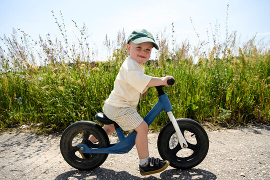 A smiling boy rides a bike on a path in a summer field