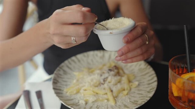 Woman sprinkling grated cheese on penne pasta at Paris cafe