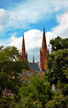 Wiesbaden, Hesse, Germany &ndash; Neo Gothic towers of Marktkirche rising above historic buildings and lush green trees under blue sky.