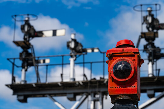 Close-up of a red railway crossing warning lamp with historic semaphore signals in the background at Grosmont, North Yorkshire, England.