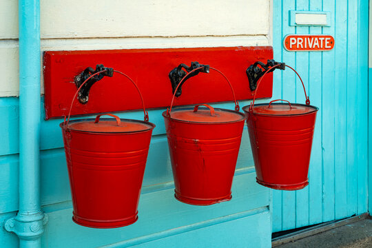 Three vintage red fire buckets hanging outside a turquoise wooden station building at Grosmont, North Yorkshire, England.