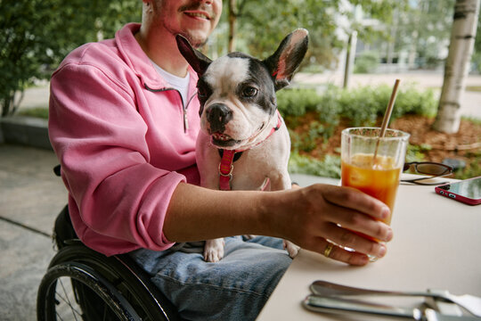 A man in a wheelchair holds a drink with his dog at an outdoor cafe