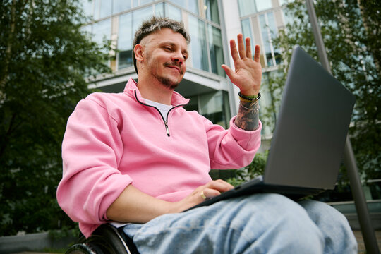 Man in wheelchair waves at laptop during outdoor video call