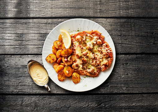 Gratinated schnitzel with cheese and potato on wooden table