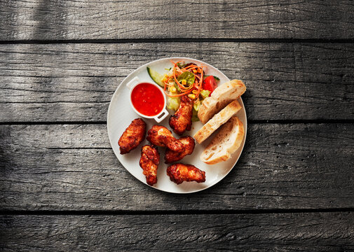 Plate of chicken wing with bread and salad on wooden table