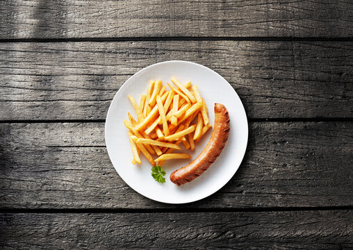 Grilled bratwurst and french fries on white plate over wooden table