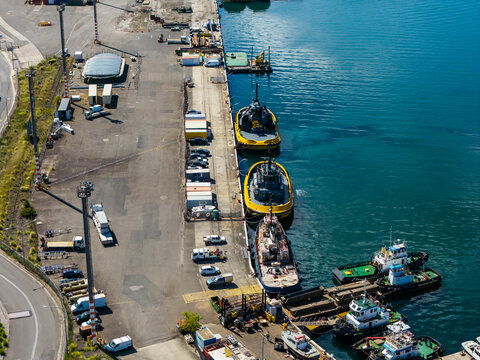 Aerial view of a working harbour with multiple tugboats moored at an industrial wharf alongside service vehicles and equipment in Rozelle, New South Wales, Australia.
