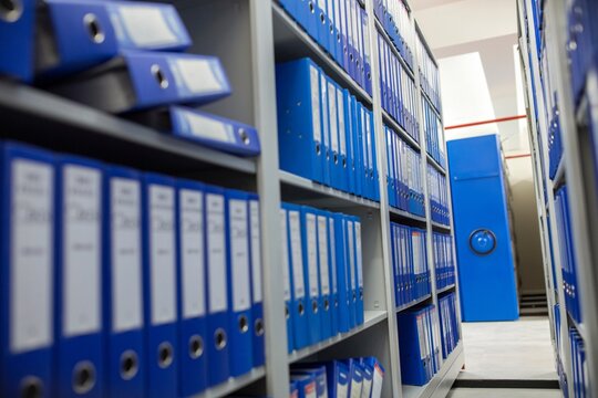 Rows of blue binder folders organized on metal library shelving units with document organization business