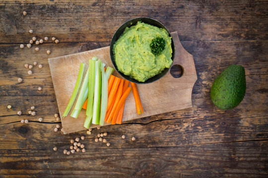 Bowl of avocado hummus, avocado, chick-peas and crudites on wood