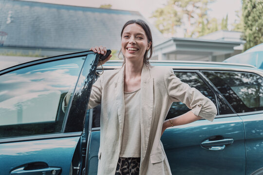 Proud woman leaning on car door holding key at home