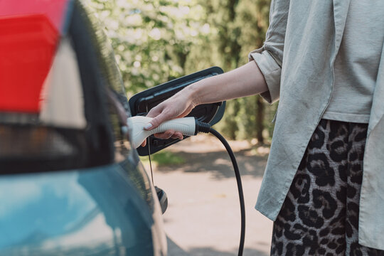 Woman plugs charging cable into electric car outdoors