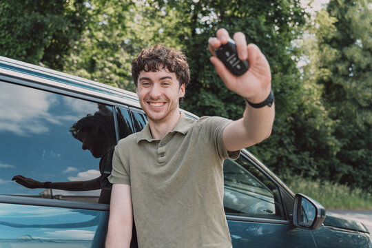 Happy man leans on a car and holds up a key outdoors