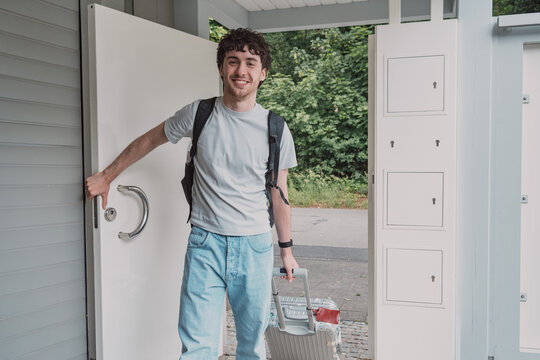 Smiling son arrives home from a trip with his suitcase and backpack