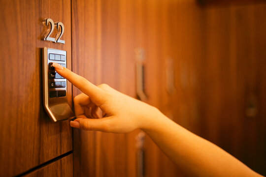 Hand pressing keypad on a secure locker with number 22 visible, wooden locker background, indicating a storage or security system in a modern facility