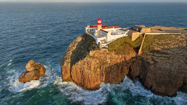 Drone view of Cabo de Sao Vicente Lighthouse in Sagres, Algarve, Portugal, with a rock stack and Atlantic cliffs at sunrise. Orbit parallax shot