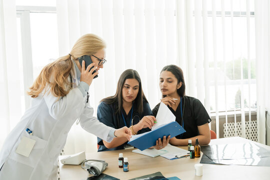 Female doctor talks on phone and reviews document with nurse indoors