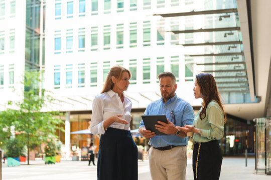 A corporate team discusses work on a tablet outdoors