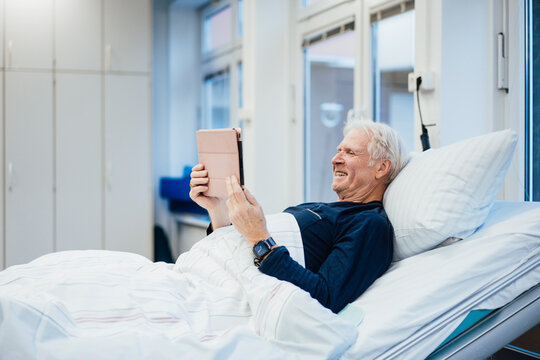 Patient in hospital bed using tablet computer and smiling