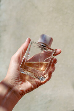 Woman holds an elegant glass perfume bottle outdoors in the sunlight
