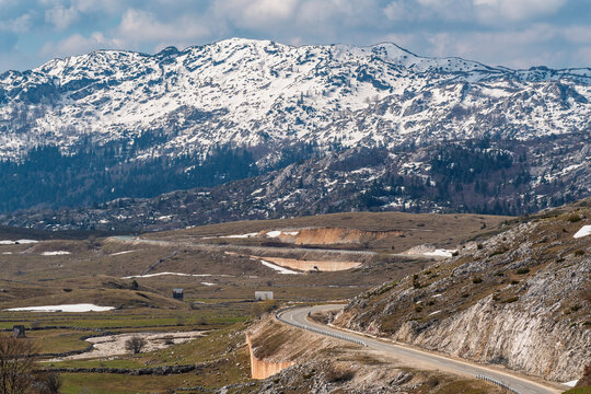 An empty road traverses the snowy Durmitor mountain valley