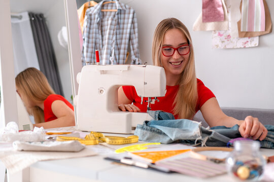 Smiling seamstress repairs denim clothing on a sewing machine indoors