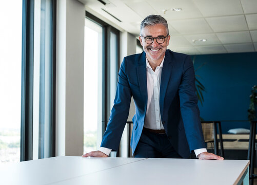 Smiling businessman leans on a table in the modern office