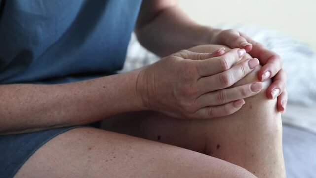 Closeup of unrecognizable female fingers massaging aching knee joint while sitting in bed