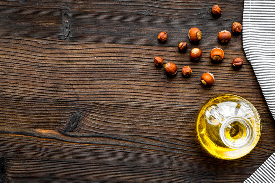 Oil as cosmetics. Haselnut oil near nut in shell on dark wooden background top view copy space