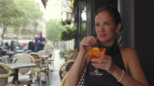 Smiling woman sipping orange drink at Paris outdoor cafe