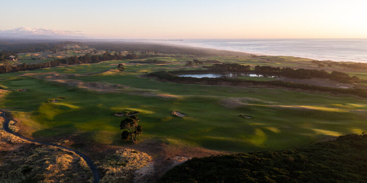 Aerial view of a rugged golf course fairway nestled along the Pacific coast during golden hour in Bandon, Oregon.