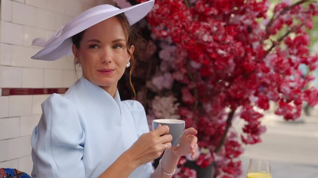 Woman in white hat sipping from cup beside flowers at Paris cafe