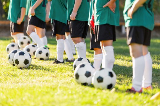 Team of Junior Soccer Players Standing in Line with Soccer Balls at Their Feet - Youth Football Squad Skill Drill and Ball Control Practice