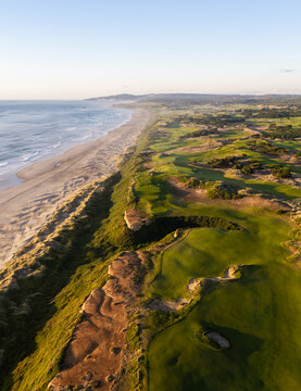 Aerial view of Bandon golf links with lush green fairways and sand bunkers along the rugged coastline and beach at sunset Bandon, Oregon, United States.