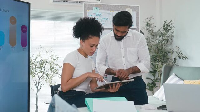 Male and female professionals analyzing business data and discussing strategy over a digital tablet and documents in a modern workspace.