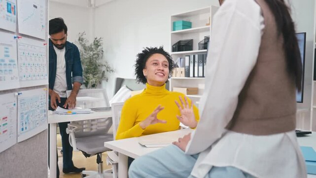 Cheerful professional businesswoman in a yellow sweater talking and gesturing during a team meeting in a modern corporate office setting.