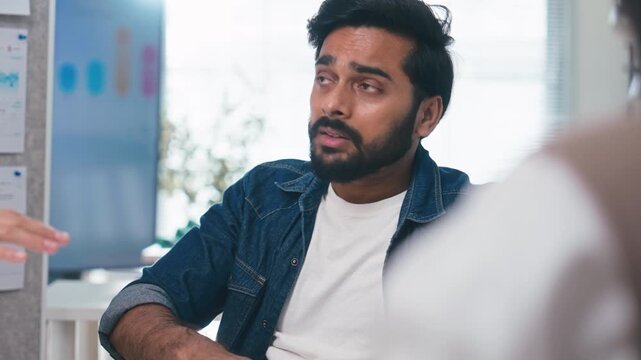Indian male business talking and gesturing during a team meeting in a modern corporate office setting.