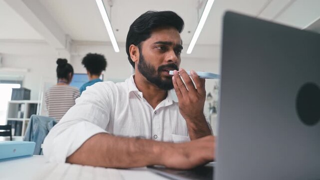 Businessman Working on Laptop and Using AI Voice Assistant on Smartphone in Office.