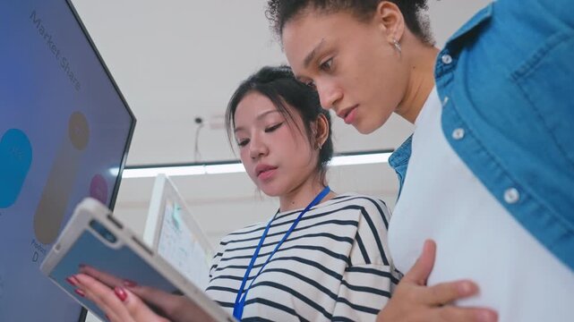 Asian and Brazilian Businesswomen Discussing Data Analysis with Tablet in Modern Office.