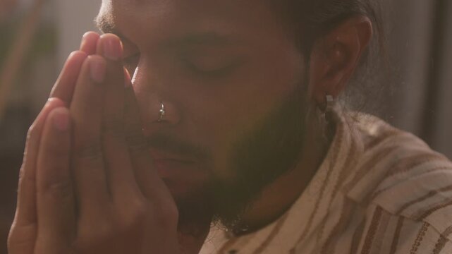 Young adult Indian man holding hands in prayer while meditating with closed eyes in close up. Footage suits mental wellness campaigns, mindfulness apps, and spiritual lifestyle advertising