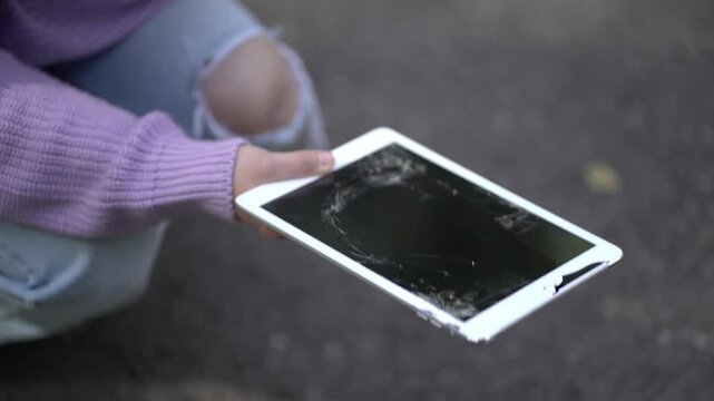 Close-up hands of a woman presenting a severely damaged tablet with a shattered display, symbolizing accident, technology failure, replacement and repair.