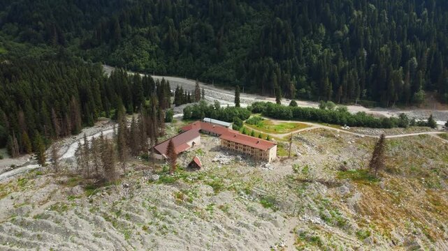 Dramatic aerial photography flying over the remnants of a devastating landslide in Georgia's remote Shovi Racha mountain valley, revealing a wide path of rocks and debris among lush green coniferous f