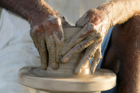 View of a potter shaping wet clay on a spinning pottery wheel with hands covered in mud in Multan, Punjab, Pakistan.