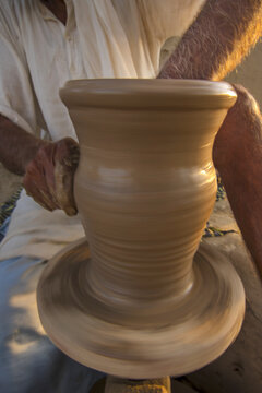 View of a skilled potter shaping a clay vessel on a spinning wheel with hands covered in mud in Multan, Punjab, Pakistan.