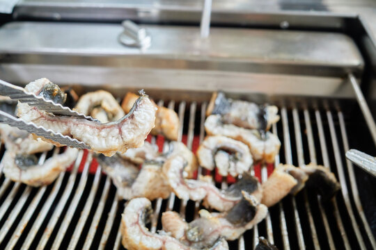 A natural close view of Ganghwa Island mud flat eel grilling over red hot charcoal embers. Highly sought after for its savory flavor kick, capturing authentic traditional Asian countryside barbecue cu