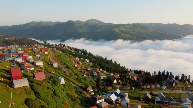 Aerial view of the stunning mountain village of Gomis mta in Georgia with bright houses nestled on a green slope above a sea of clouds at dawn, showcasing a calm and picturesque landscape