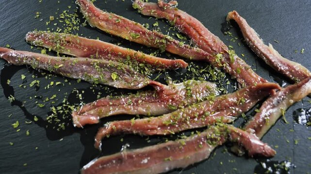 Marinated anchovy fillets sprinkled with chopped herbs arranged on a dark slate surface. High quality 4k footage