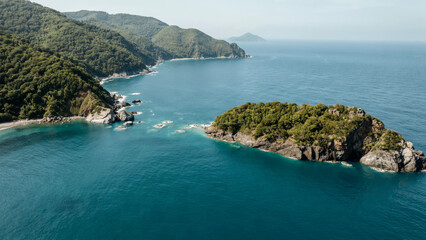 Obraz premium Aerial view of lush green mountains meeting turquoise ocean waters near rocky coastline.