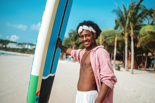 Smiling happy young black man enjoys a sunny day paddling, surf on a tropical beach resort