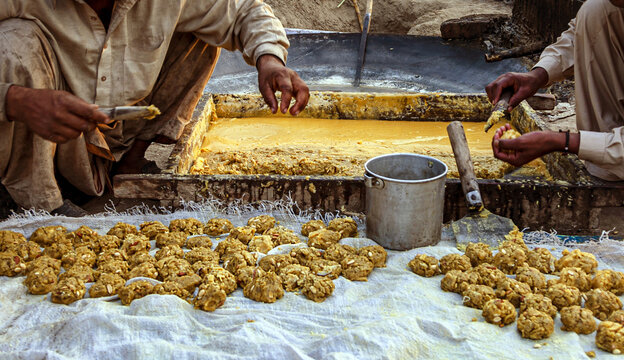 View of workers shaping traditional jaggery into small balls from a large pan in Multan, Punjab, Pakistan.
